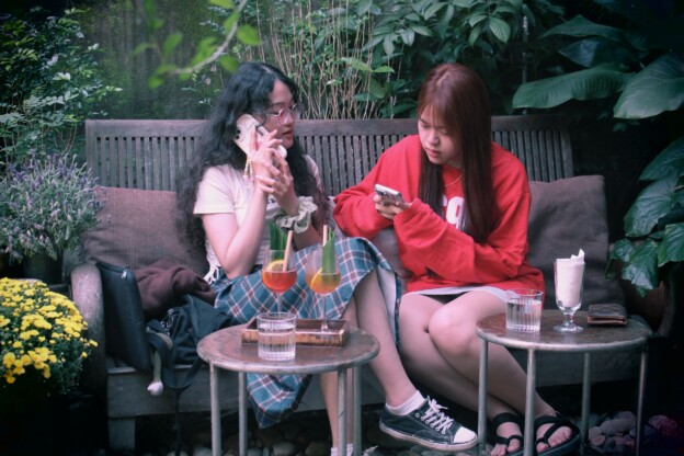 Two Korean people talking at a café while one holds a smartphone