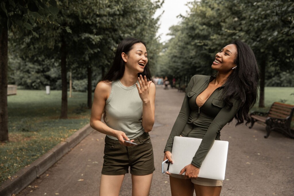 Two Korean friends laughing together on a park bench on a sunny day