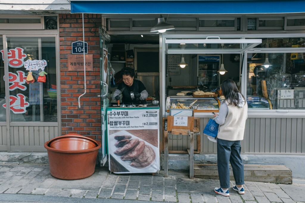 A young Korean woman ordering from an older Korean vendor at a lively food stall