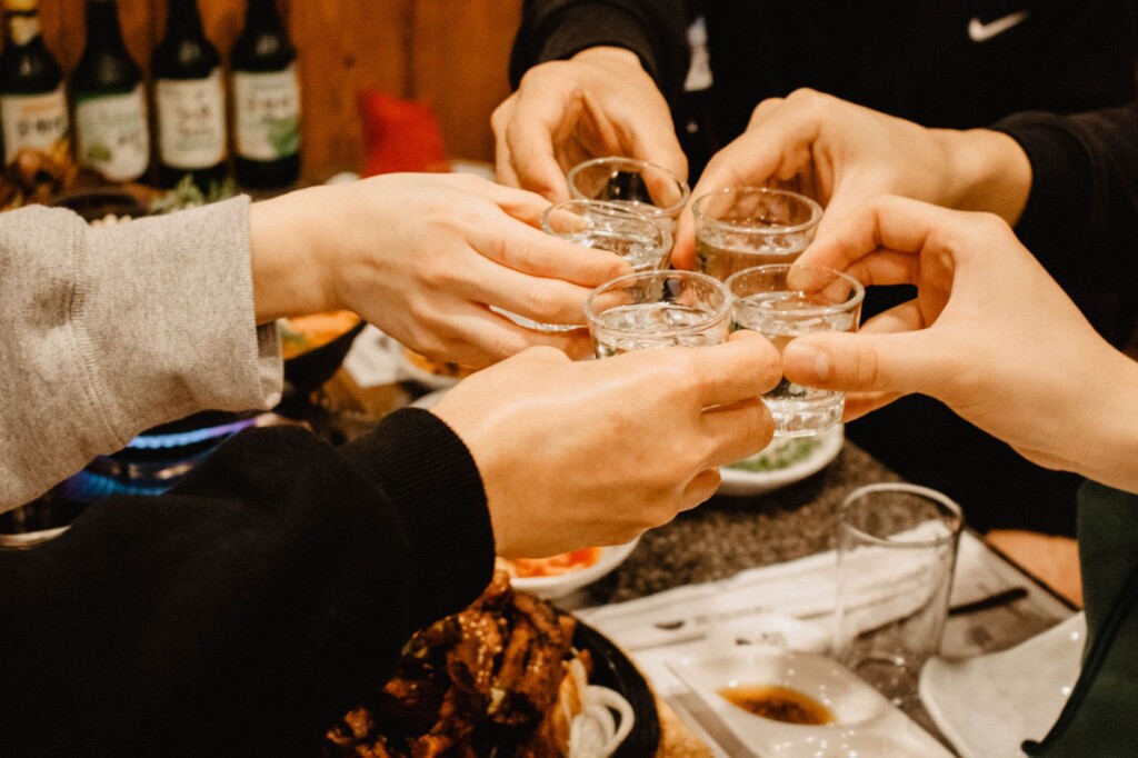 Two Korean friends toasting with glasses at a warmly lit restaurant table